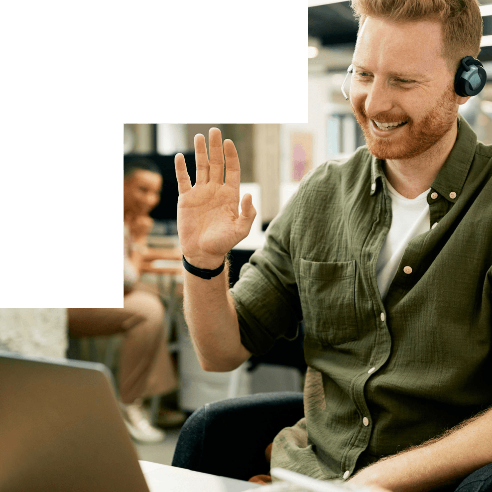 Lächelnder Mann mit Headset winkt während eines Video-Calls am Laptop im Büro.