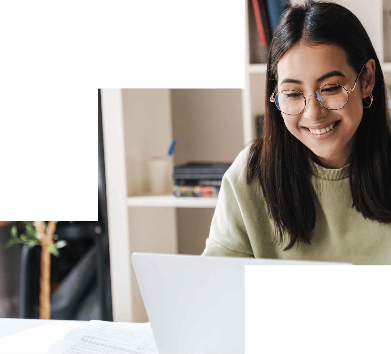 Lächelnde Studentin mit Brille arbeitet am Laptop in einem hellen Arbeitsraum.