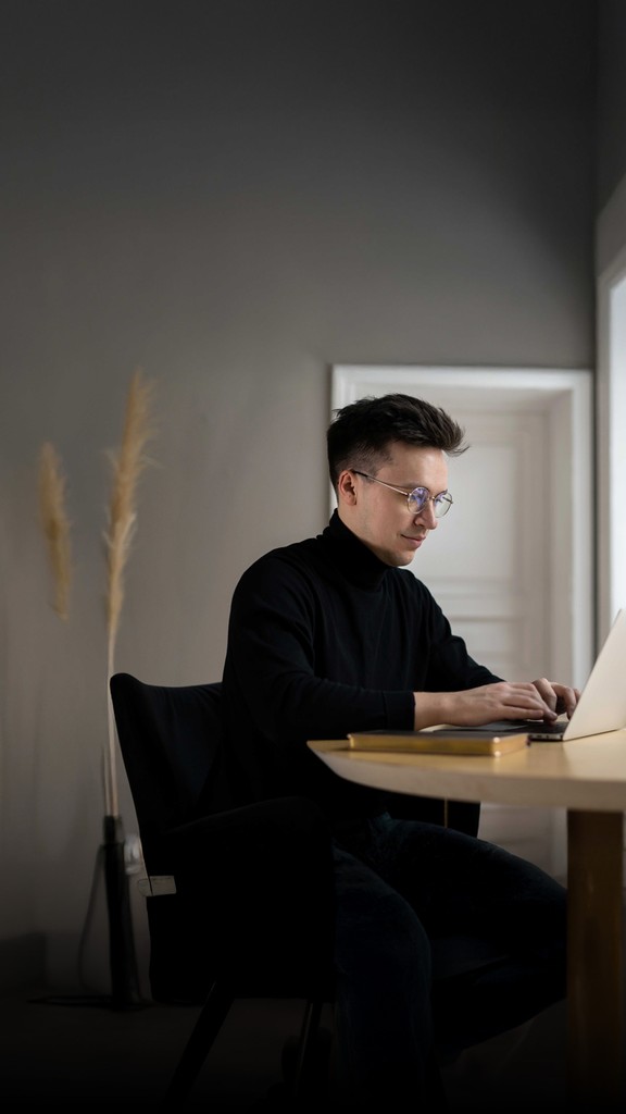 Person im schwarzen Rollkragenpullover arbeitet am Laptop in einem ruhigen Raum.