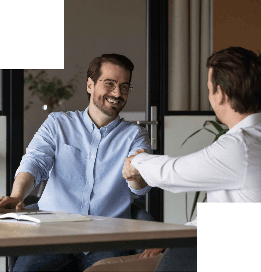 Zwei Personen geben sich lächelnd die Hand in einem hellen Büro.
